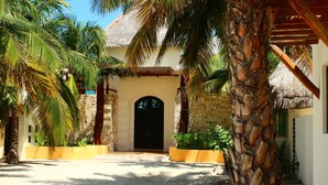 Um resort tropical com entrada de telhado de palha, palmeiras e uma parede de pedra.