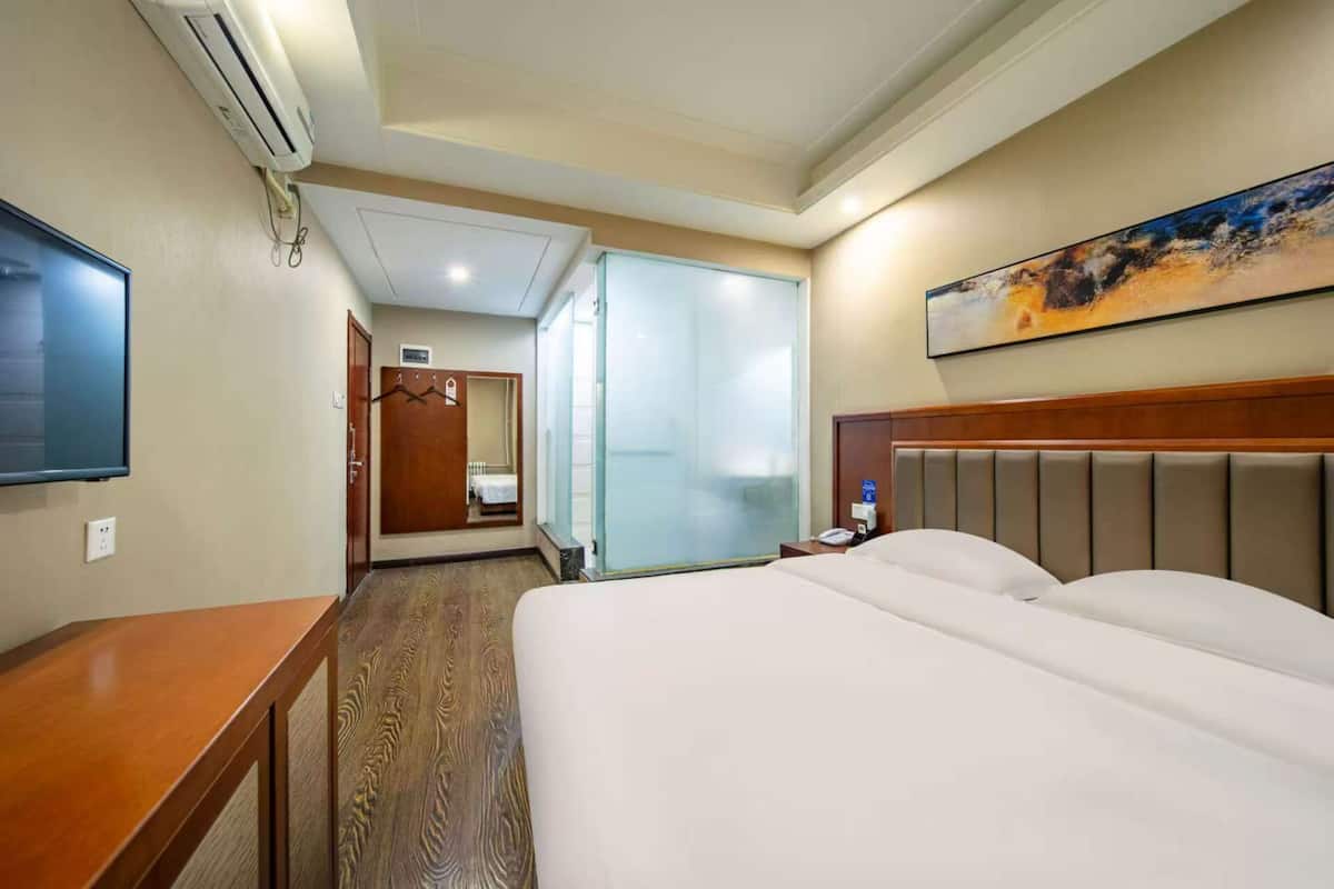 A hotel room with a bed, a desk, a mirror, and a painting on the wall.