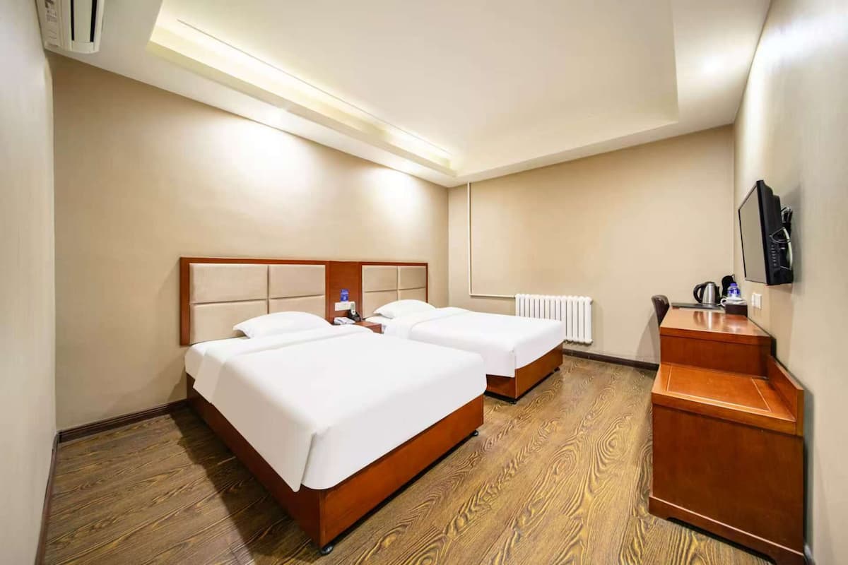 A hotel room with two beds, a wooden desk, a radiator, and a television on the wall.