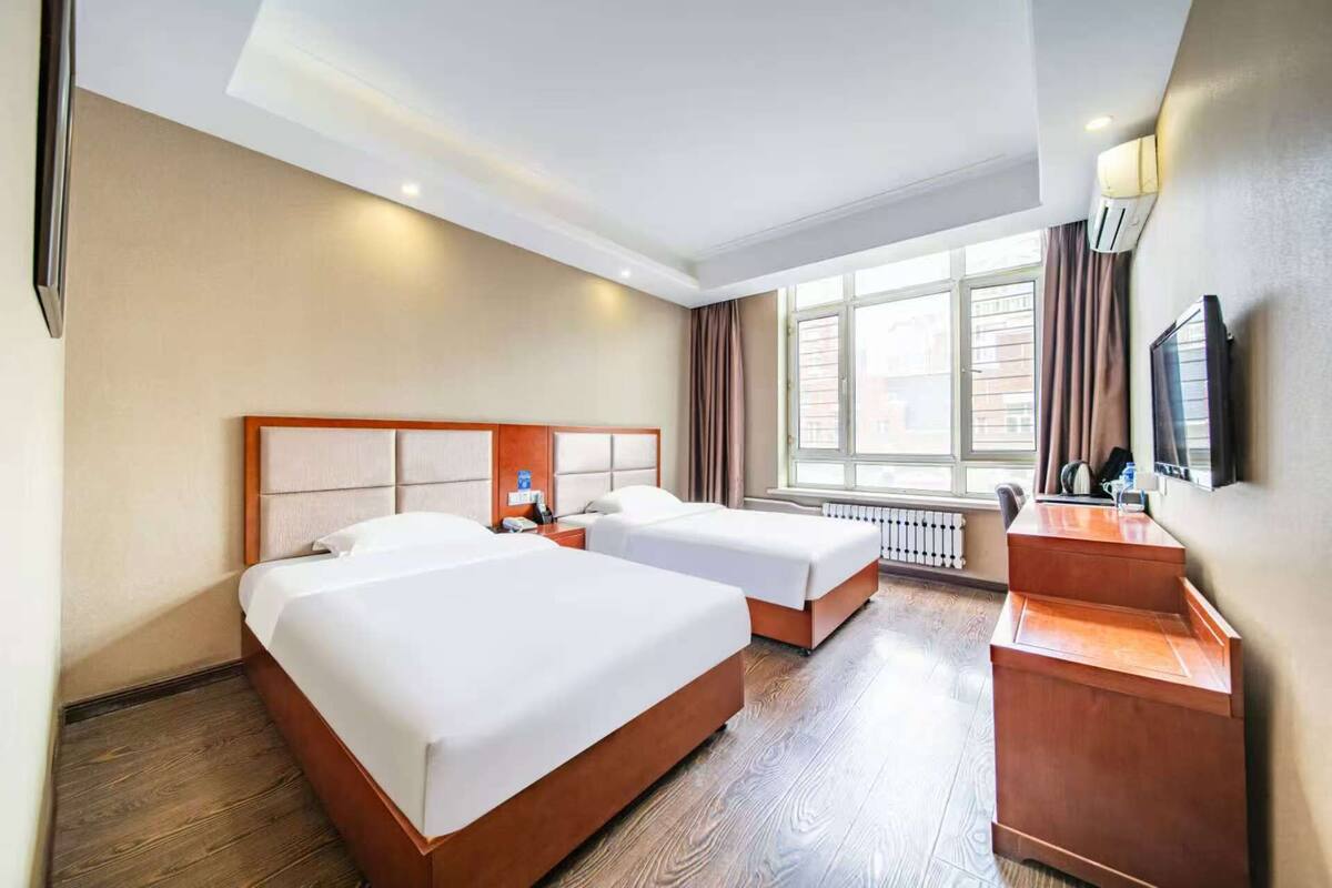 A hotel room with two beds, a desk, a television, and a window with curtains.
