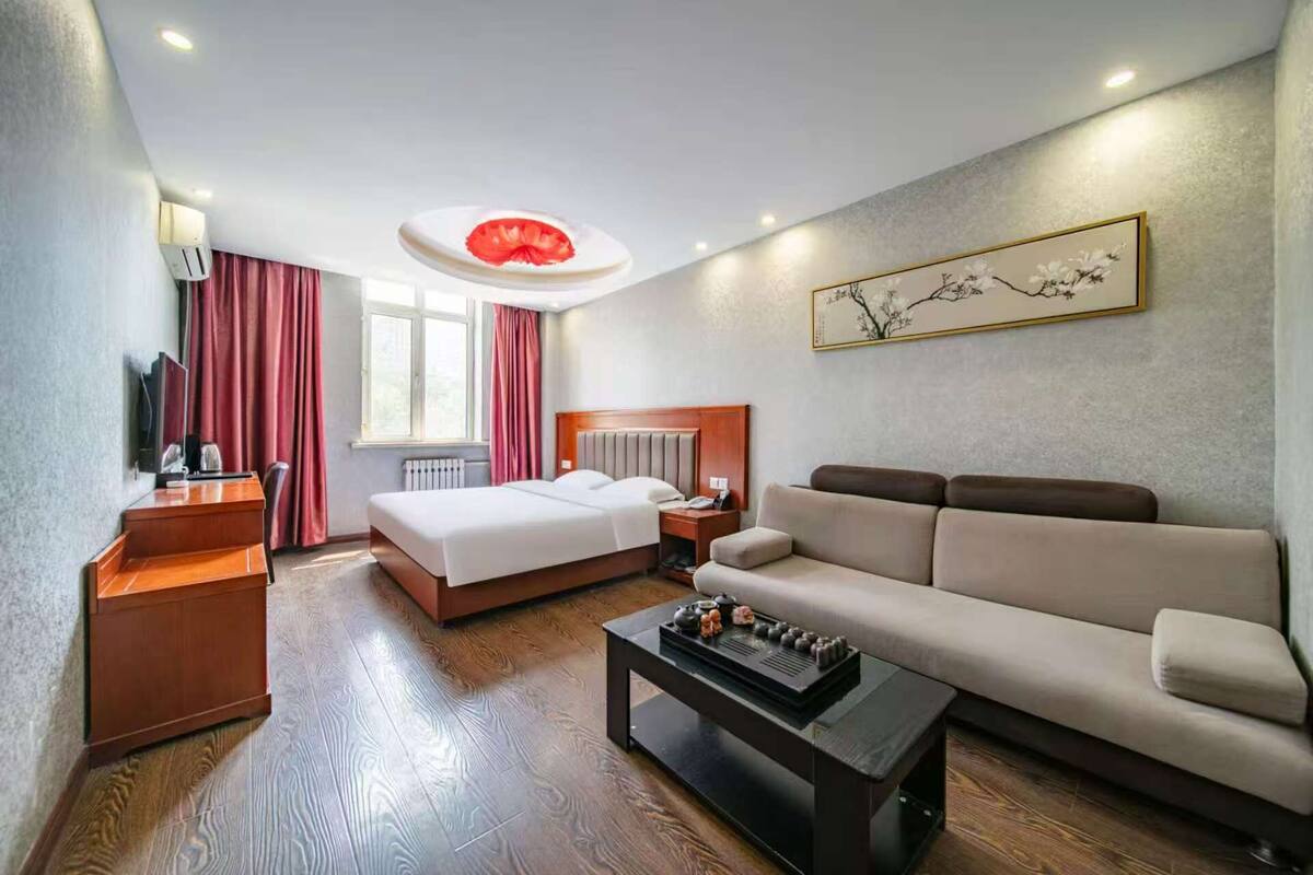 A hotel room with a bed, a sofa, a coffee table, a TV, and a window with curtains.