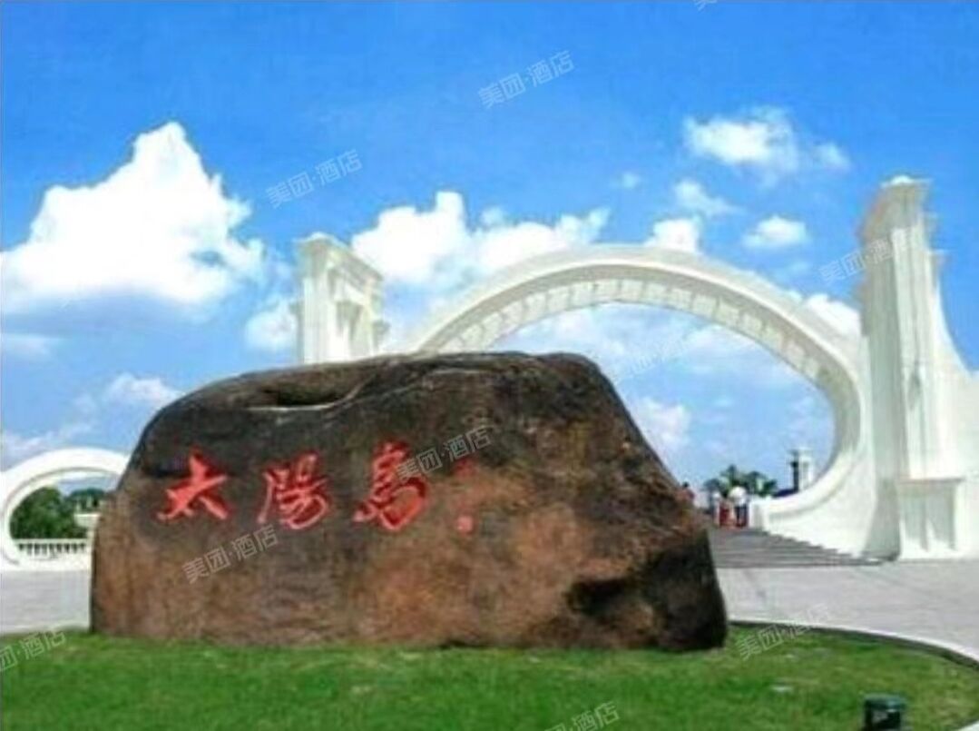 A large rock with red text in a park setting with a white arch structure in the background.