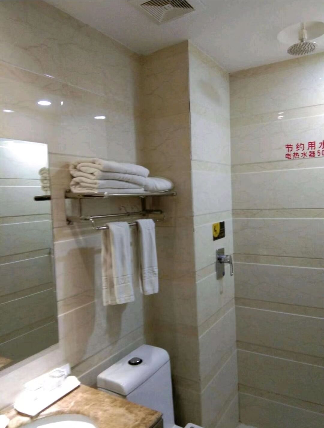 Un baño con inodoro, lavamanos, espejo y toallero con toallas dobladas.