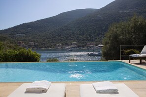 Una piscina con sillas de descanso y toallas, con vista a una masa de agua con barcos y edificios al fondo.