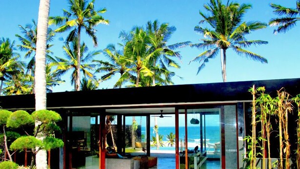 Une maison moderne dotée de grandes baies vitrées, d’un patio et offrant une vue sur l’océan.