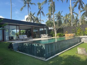 A modern house with a swimming pool, lounge chairs, and palm trees. - Beachfront Villa Inca- Breakfast included (Tabanan)