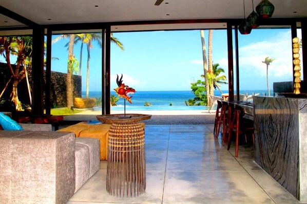 A modern interior with a large glass window offering a view of the ocean and palm trees.