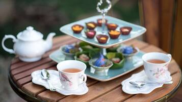 A tea set on a round wooden table with a teapot, two cups, and a tiered tray with cupcakes.