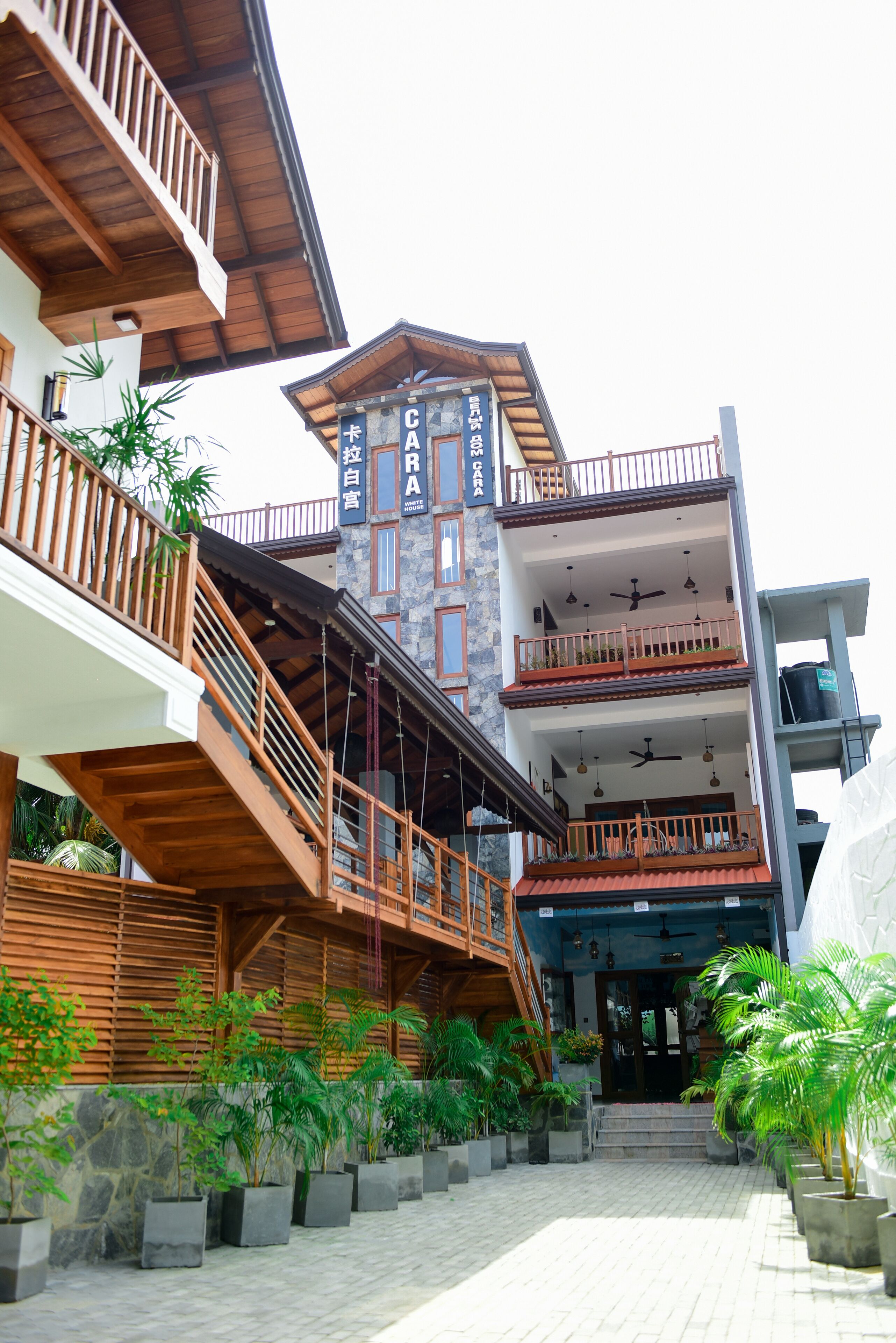 Un immeuble à plusieurs étages, doté d’un escalier en bois menant à un balcon, lequel est entouré de plantes en pot.