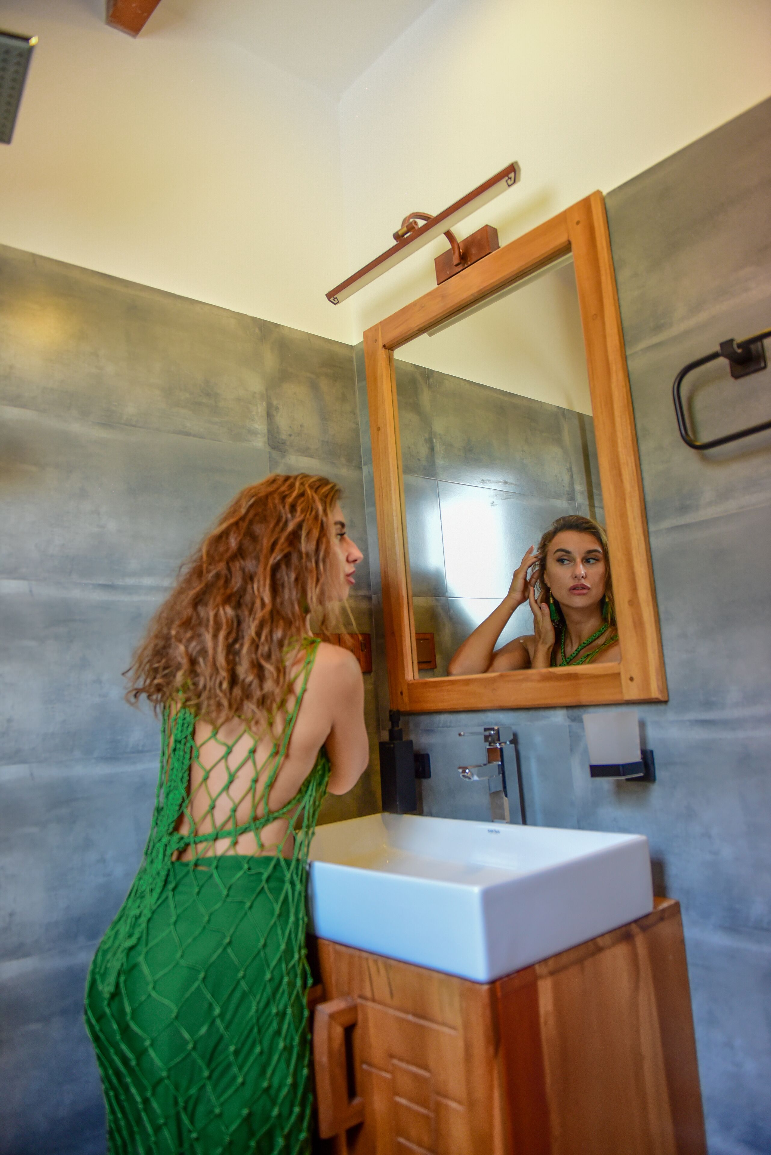 A bathroom with a wooden vanity, a mirror, and a textured wall.