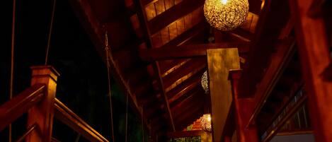 A wooden bridge with a railing, a hanging light fixture, and a staircase leading to a higher level.
