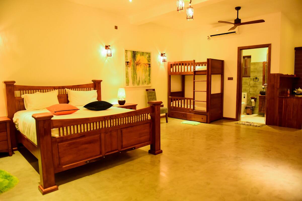 A bedroom with a wooden bed, bedside tables, a nightstand, a ceiling fan, and a painting on the wall.