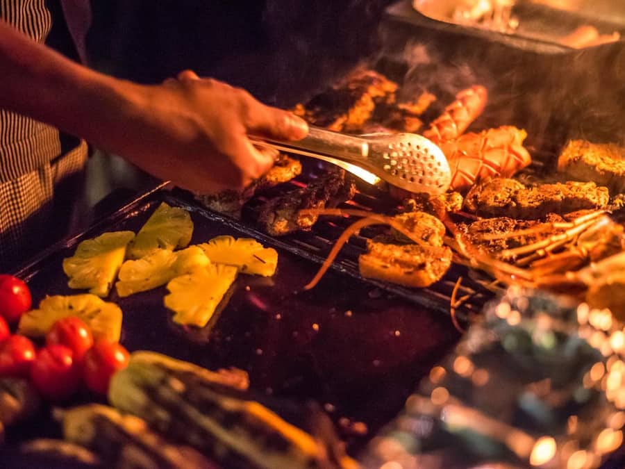 Alguém grelhando carnes e legumes na churrasqueira.