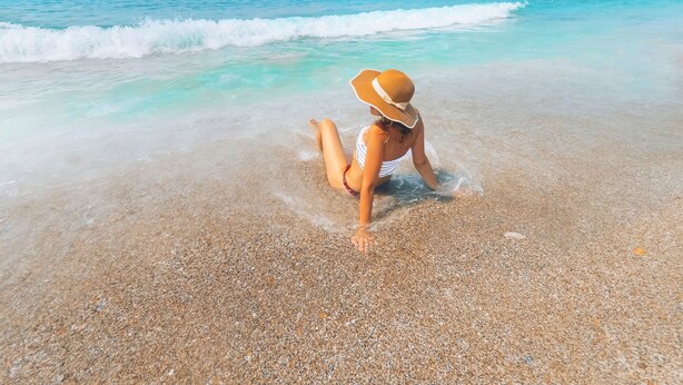A woman sitting on a pebble beach with clear turquoise water and a distant hill. - Grand Alisa Hotel – Ex.Royalisa Hotel (Alanya)