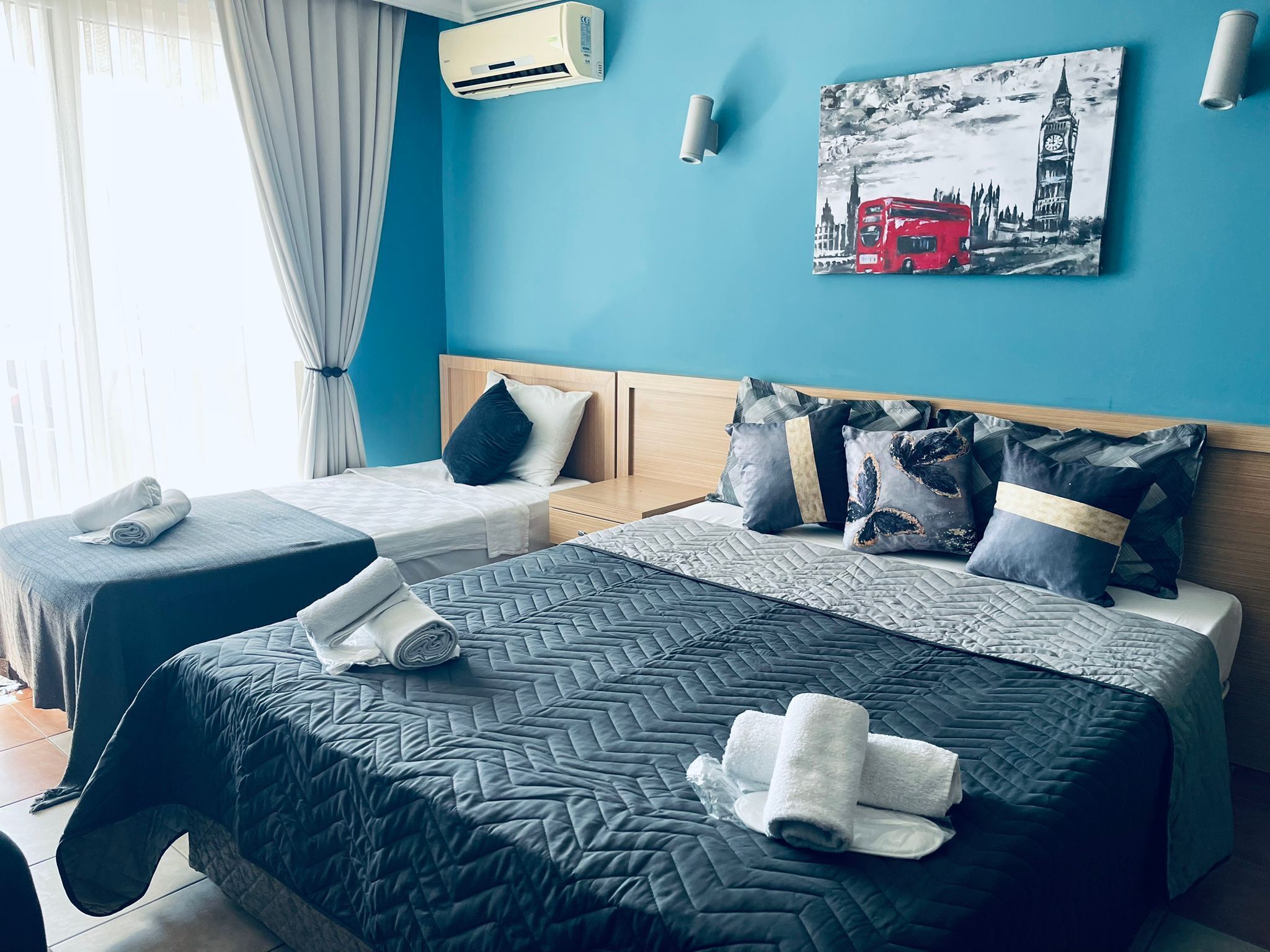 Une chambre d’hôtel avec deux lits, un tableau représentant un autobus rouge et un appareil de climatisation fixé au mur.