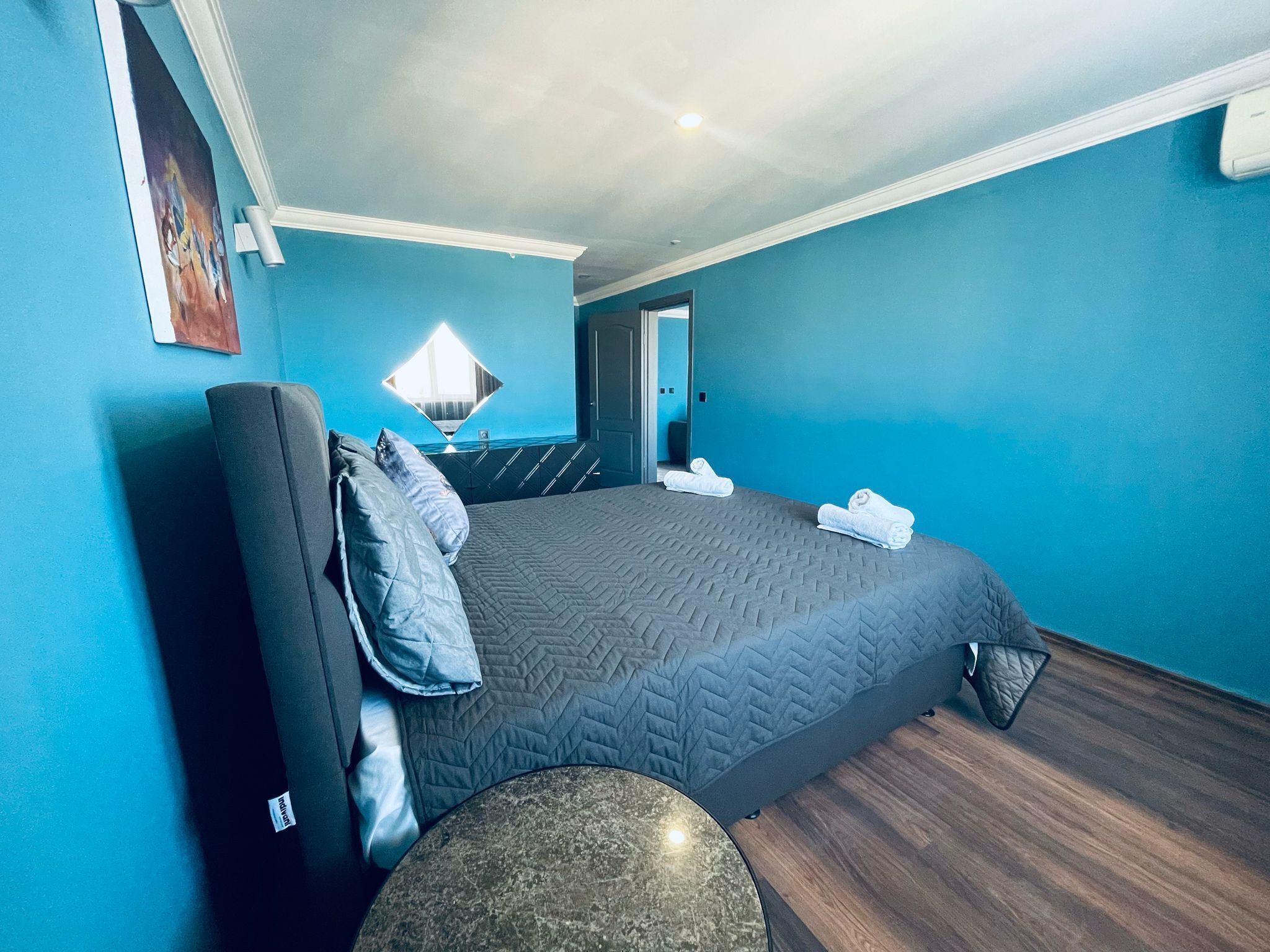 A modern hotel room with a large bed, a round table, and a view of the ocean through a window.
