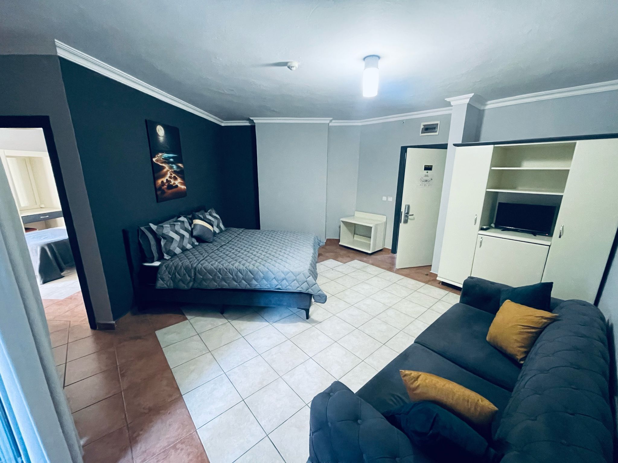 A compact living space with a bed, a sofa, a television, and a kitchenette area.