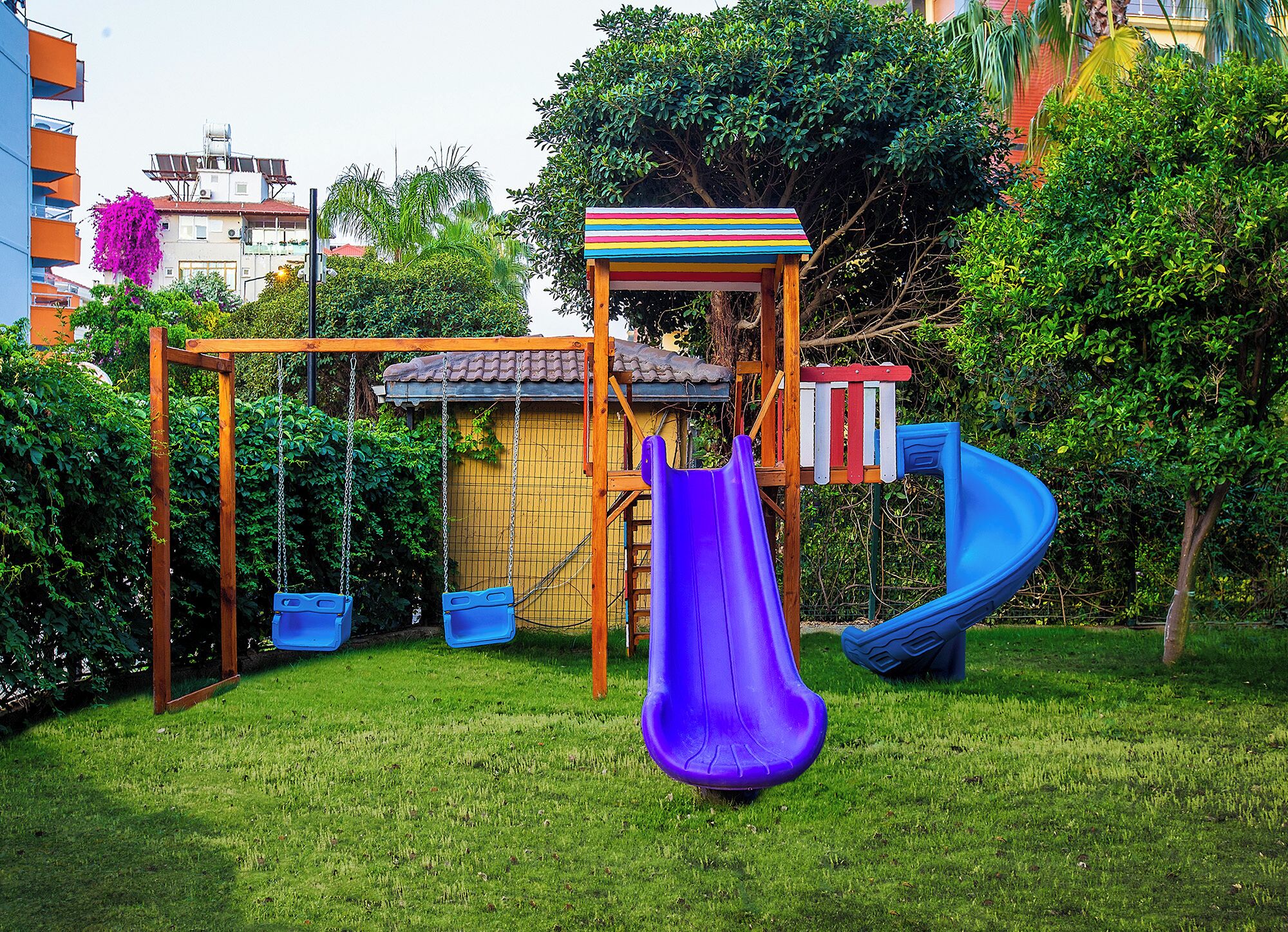 A playground with a swing set, a slide, and a small playhouse.