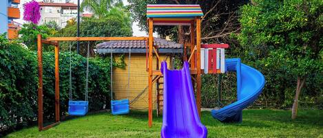 Un parque infantil con columpios, un tobogán y una casita de juegos.