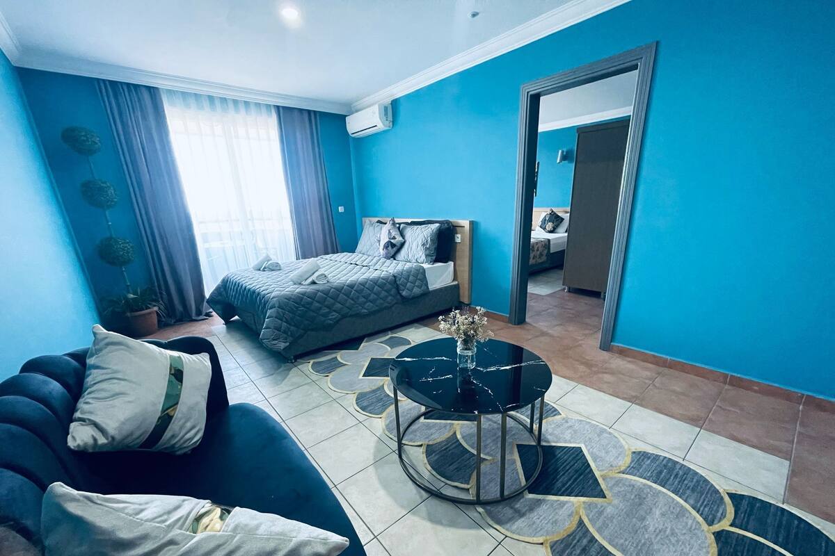 A modern hotel room with a bed, a sofa, a coffee table, and a potted plant.