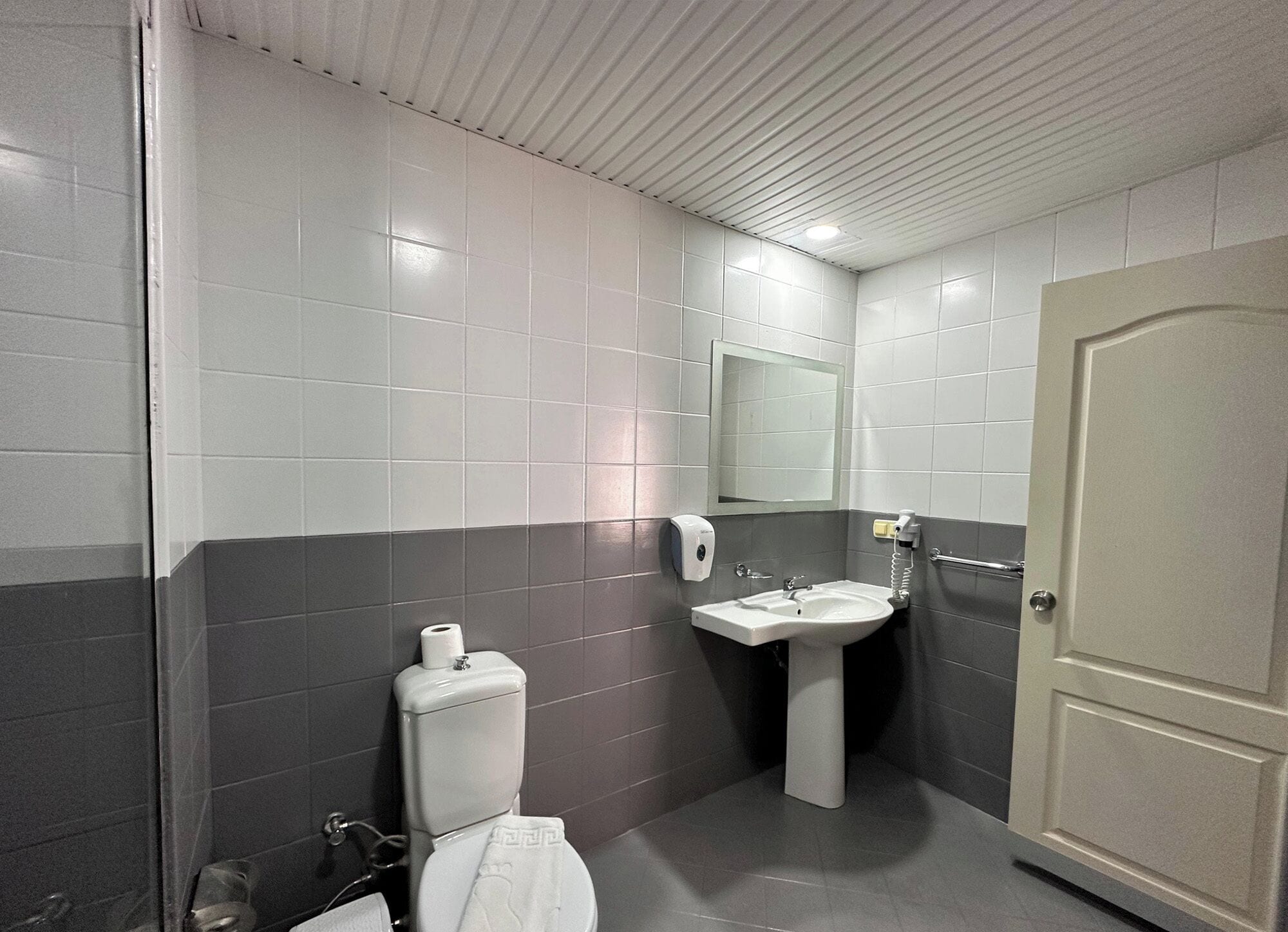 A bathroom with a toilet, sink, mirror, and towel dispenser.