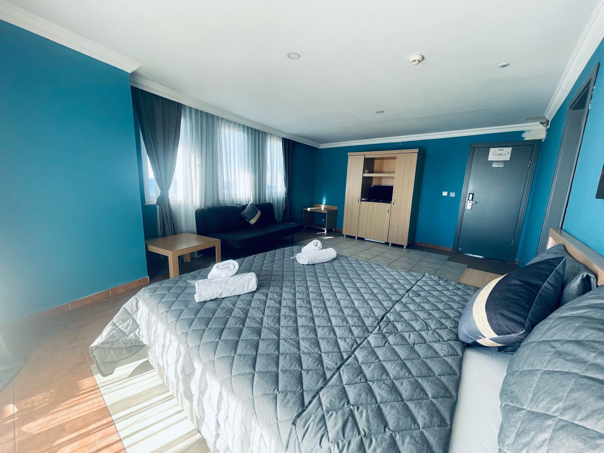 Una habitación de hotel con una cama grande, un sofá, una mesita y un armario.
