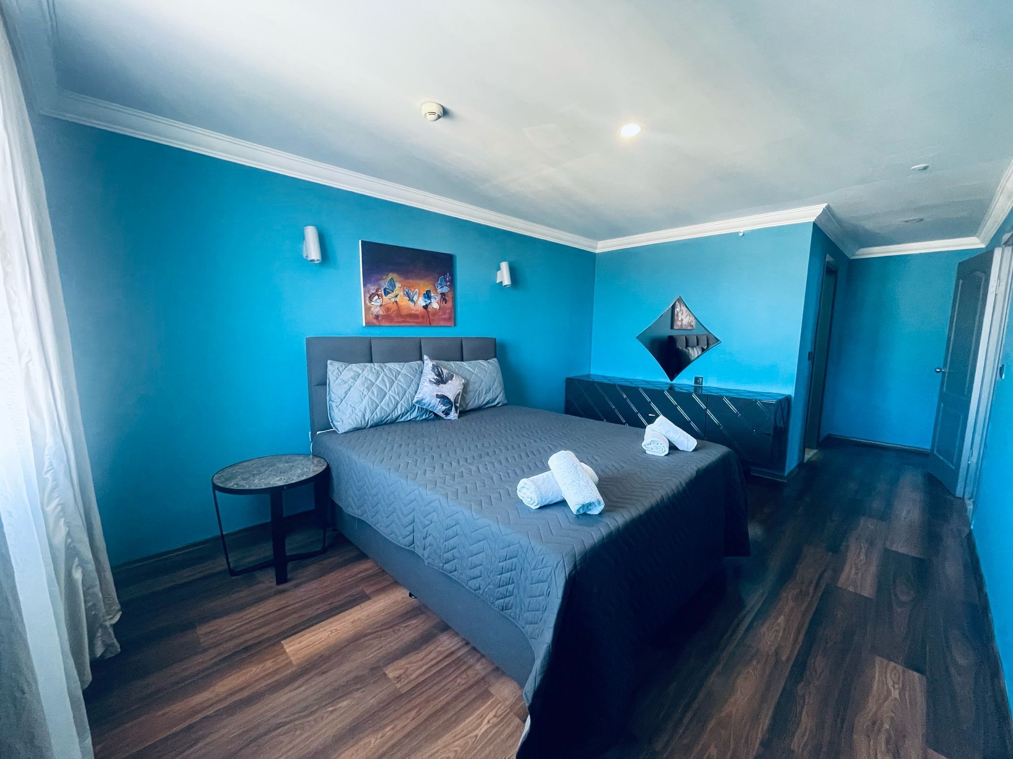 A bedroom with a bed, a small round table, and a painting on the wall.