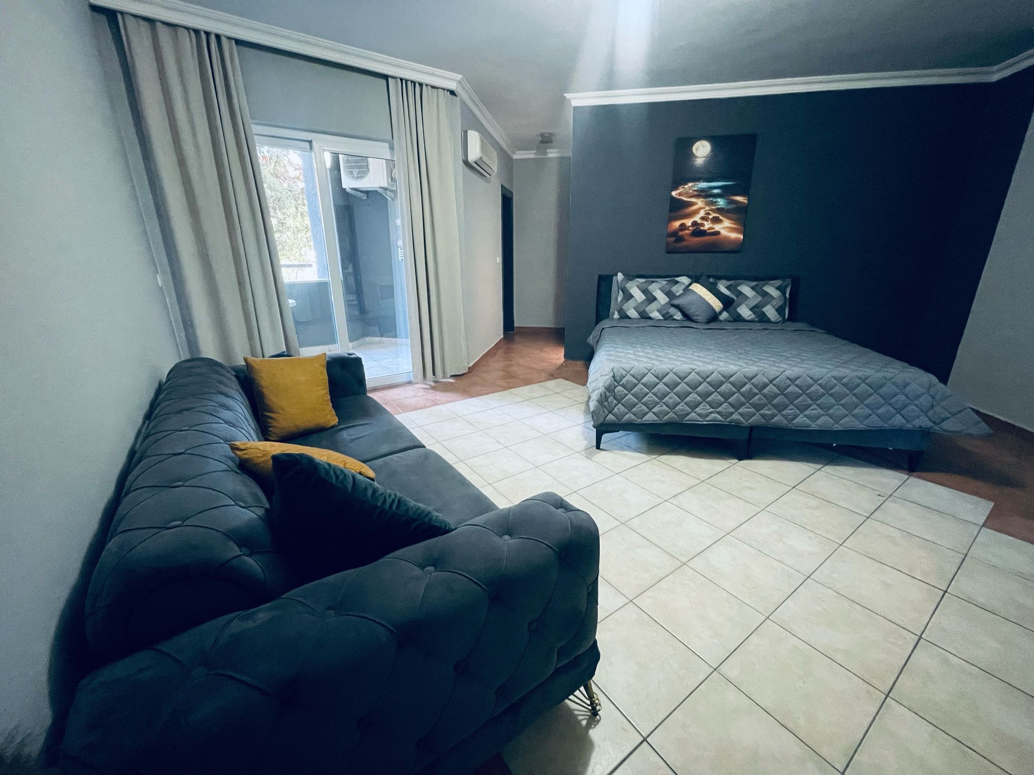 A modern bedroom with a bed, a sofa, and a sliding glass door leading to a balcony.