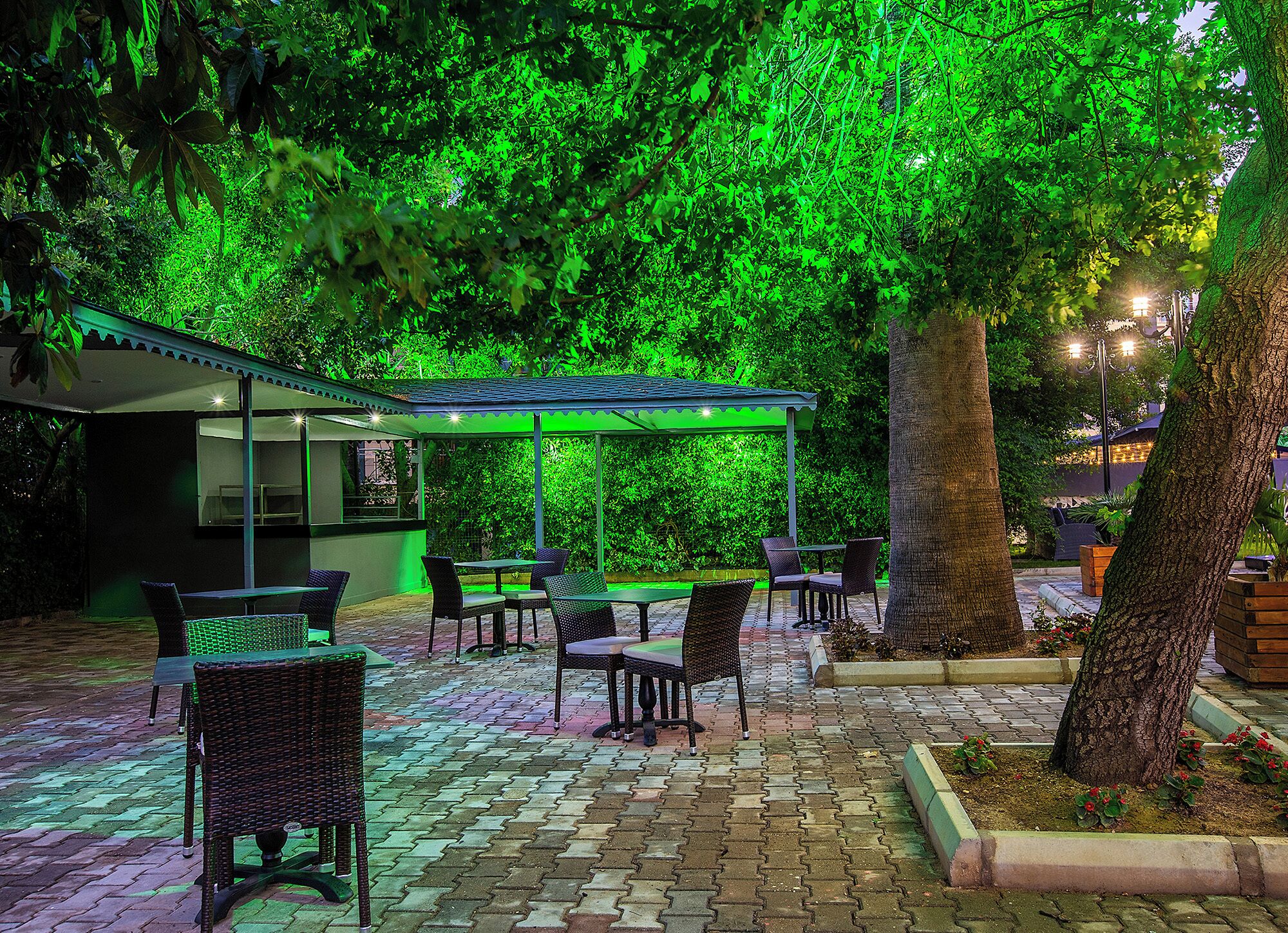 Un espace extérieur aménagé en terrasse avec des tables et des chaises, un coin salon abrité et un bâtiment doté d’un mur en verre.