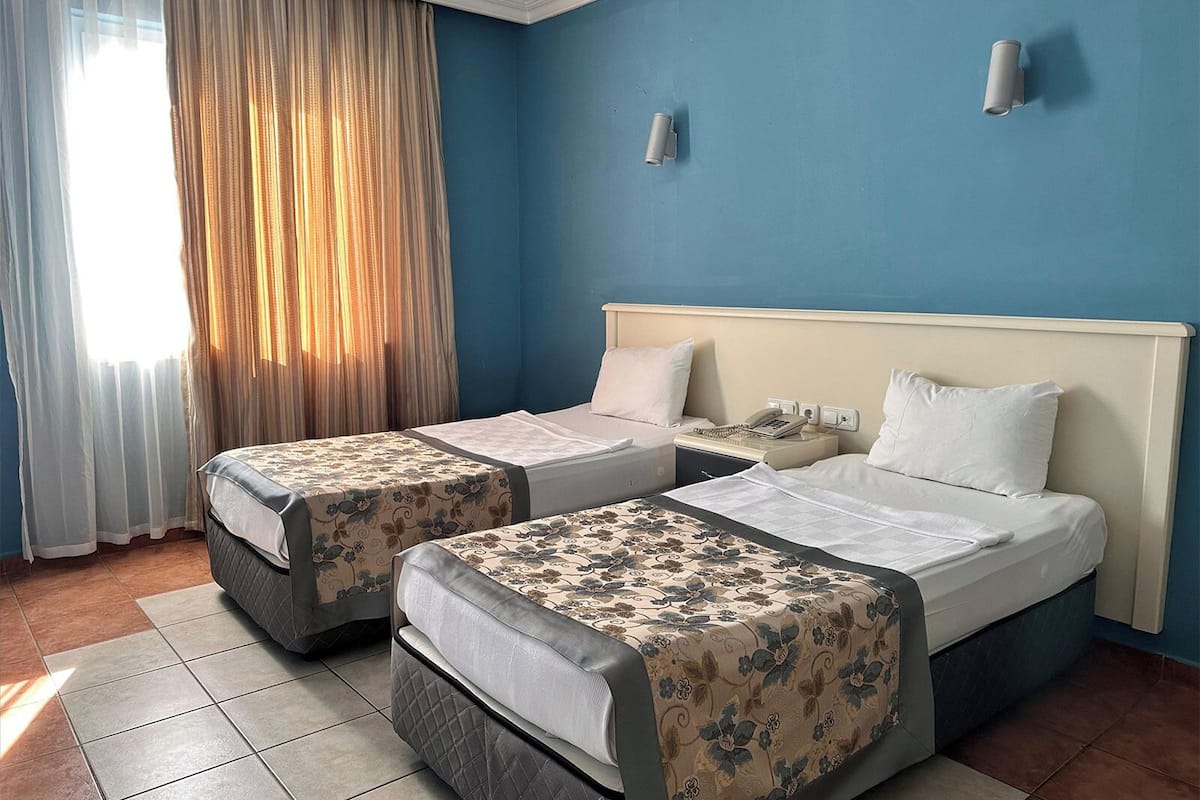 A hotel room with two beds, a nightstand, a telephone, and a window with curtains.