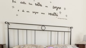 Siististi pedattu sänky, jossa on violetti nauha, seinä, jossa on kannustava sitaatti, ja yksinkertainen metallinen sängynpääty.