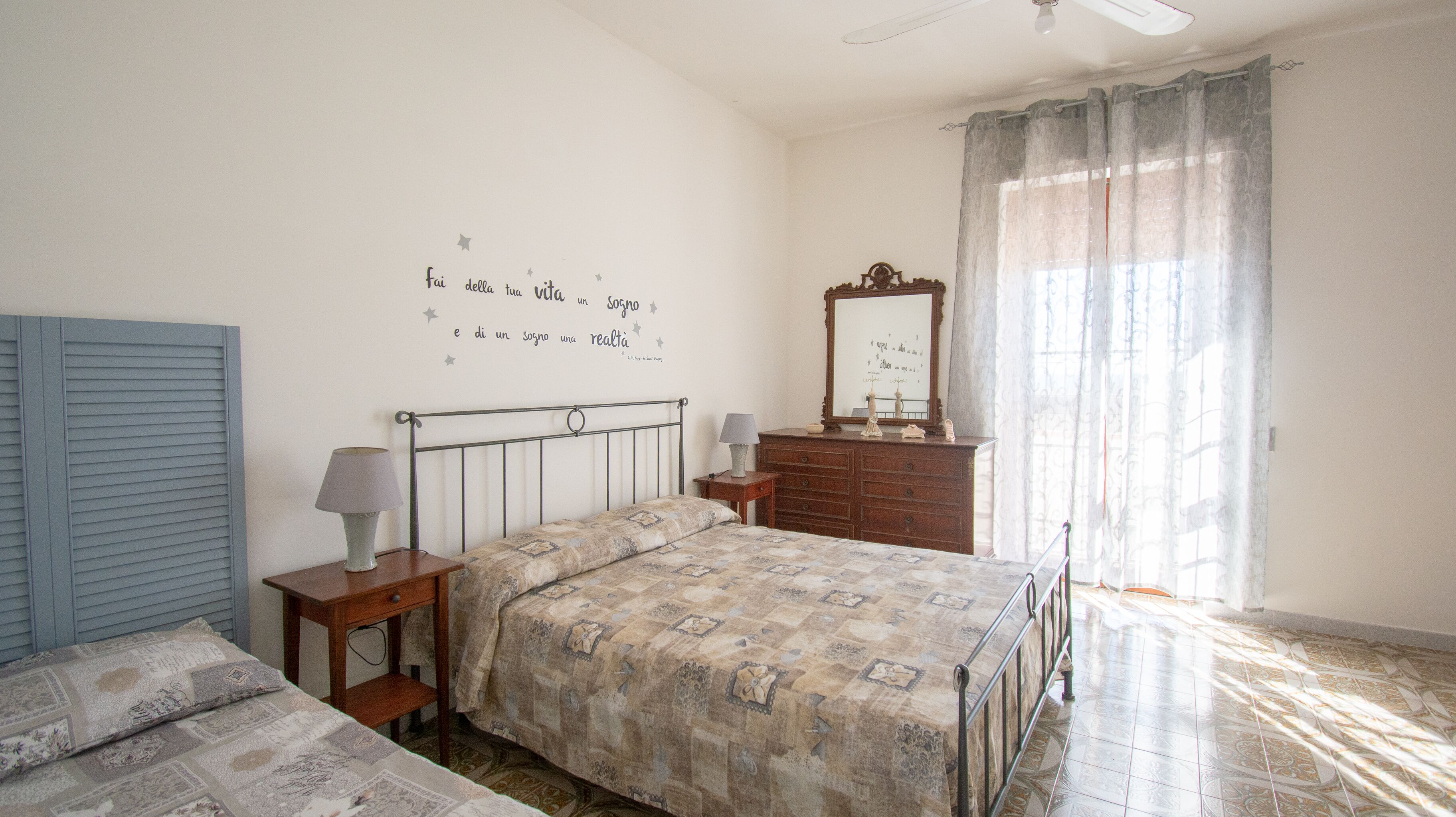 A bedroom with a bed, a dresser, a nightstand, a mirror, and a wall with a decorative phrase.