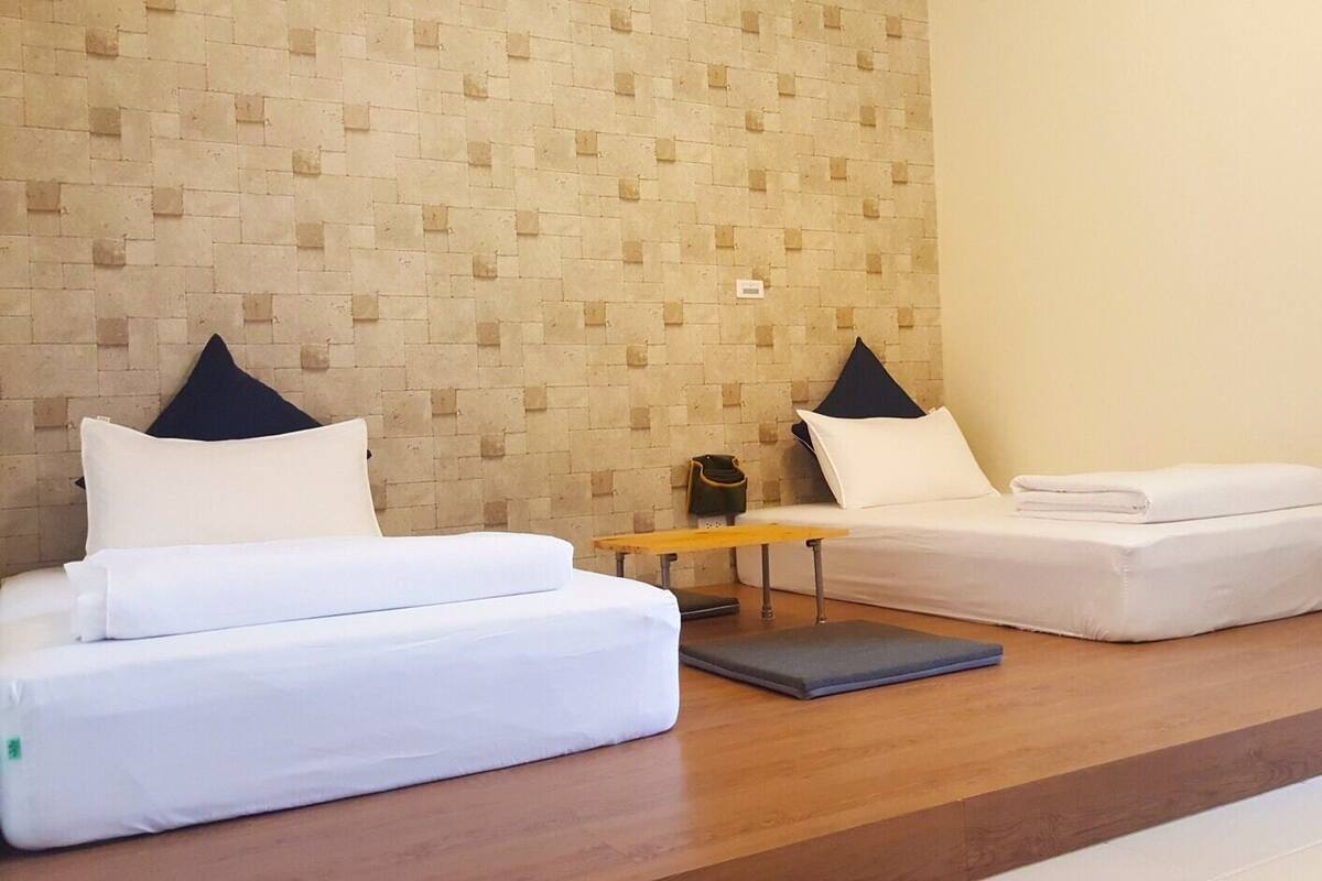 Habitación de hotel con dos camas, un banco de madera y una mesita con un bolso encima.