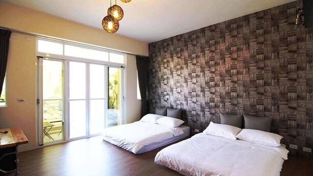 Habitación de hotel con dos camas, suelo de madera, un amplio ventanal corredero que da a un balcón y una pared con textura.