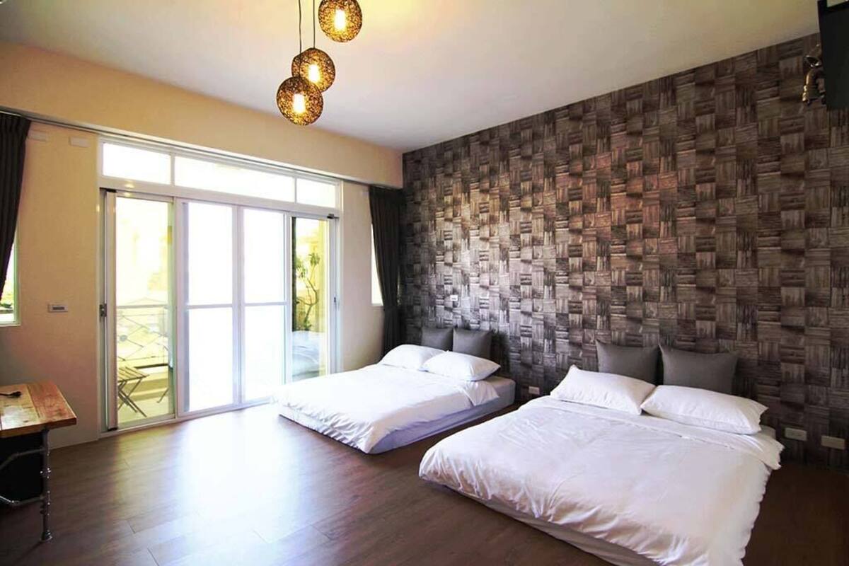 Habitación de hotel con dos camas, suelo de madera, un amplio ventanal corredero que da a un balcón y una pared con textura.