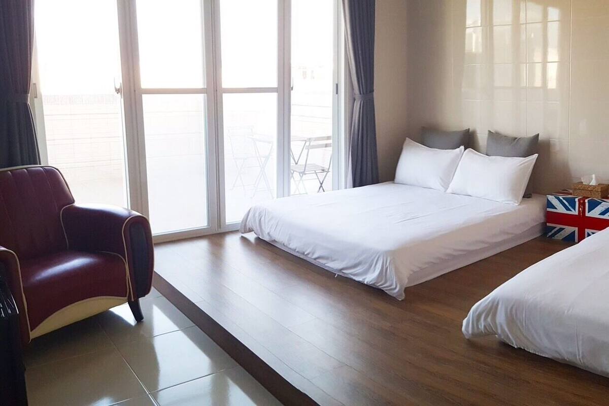 Una habitación de hotel con dos camas, un sillón rojo y una ventana con cortinas.