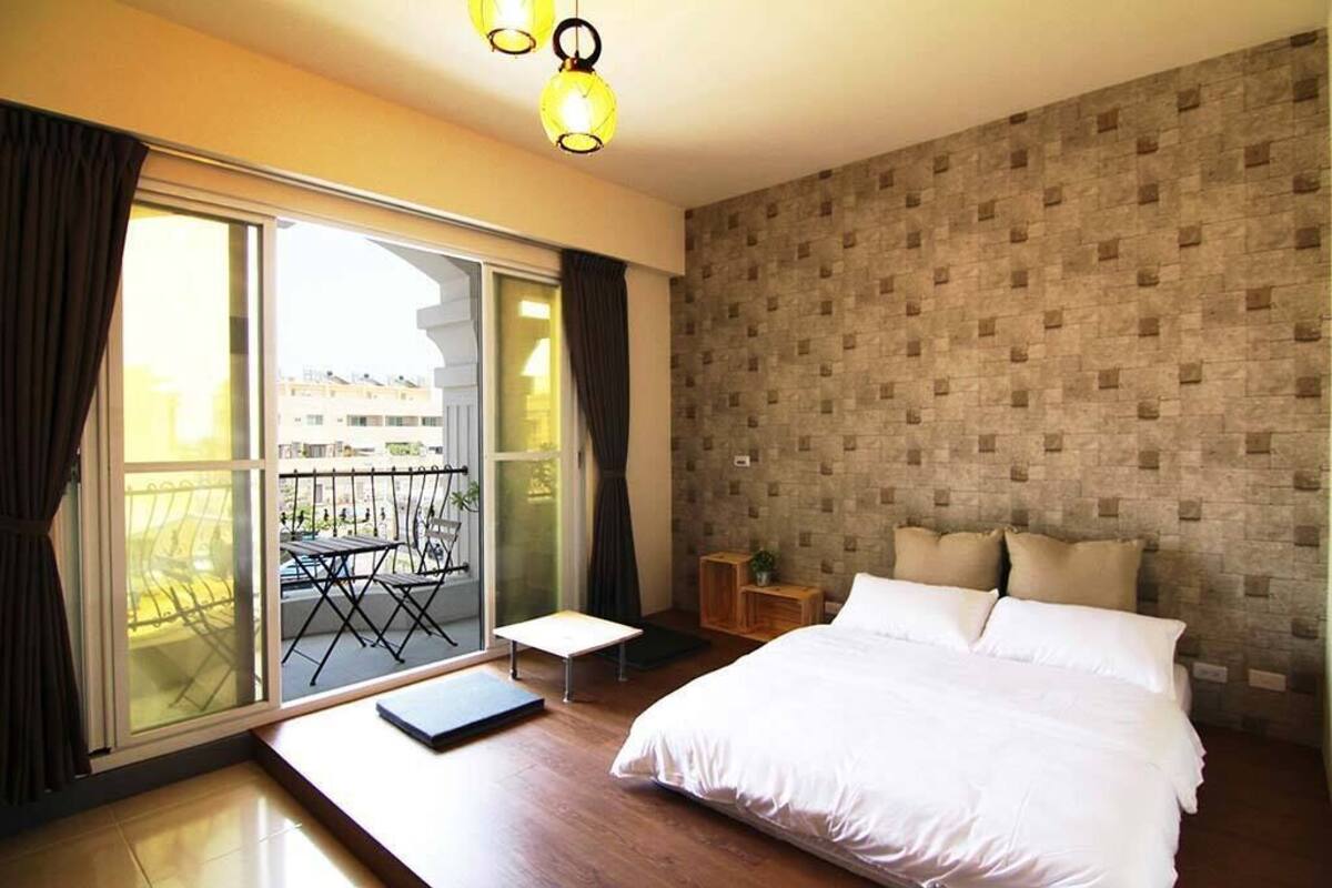 Un dormitorio con una cama grande, una mesita de noche pequeña, una ventana con cortinas y un balcón con mesa y sillas.