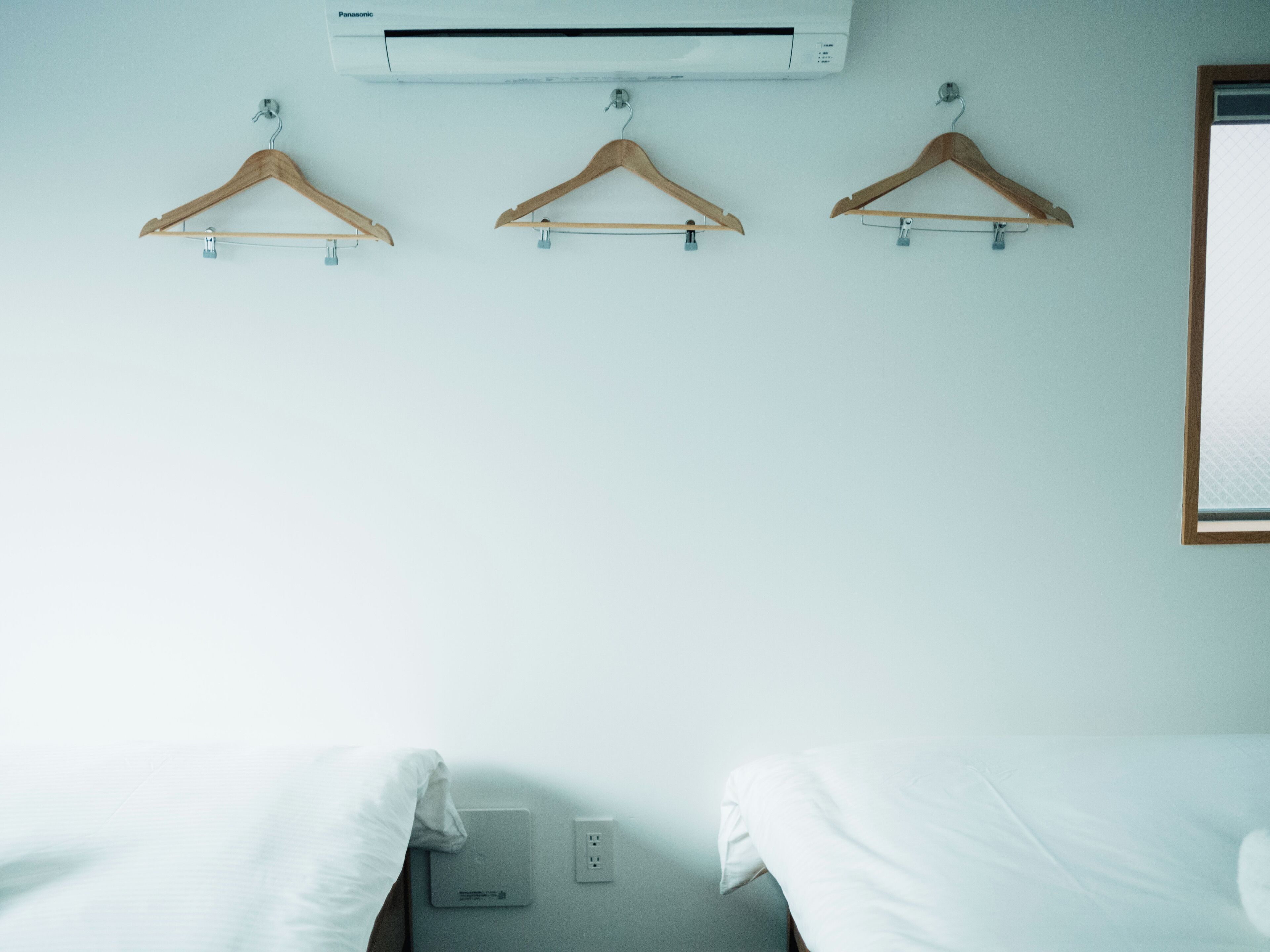 A hotel room with a bed, an air conditioner, and three wooden hangers on a wall.