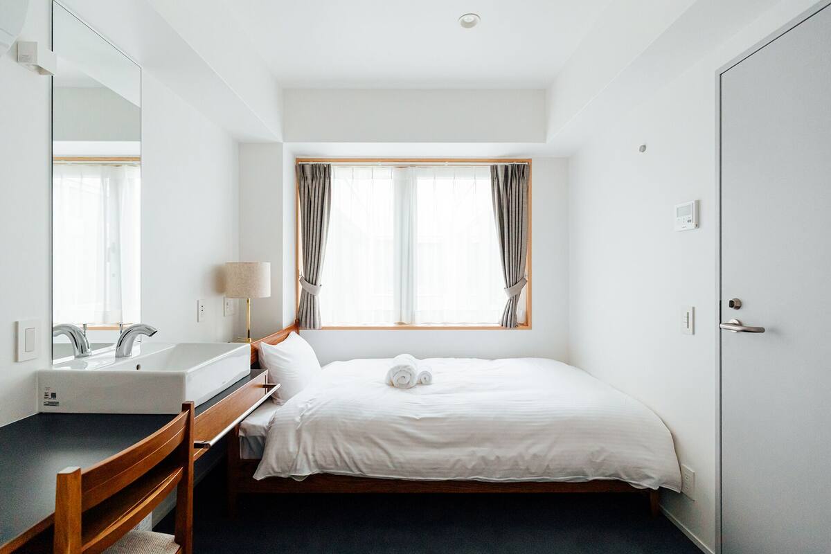 A hotel room with a bed, a bedside table, a mirror, a window with curtains, and a door.
