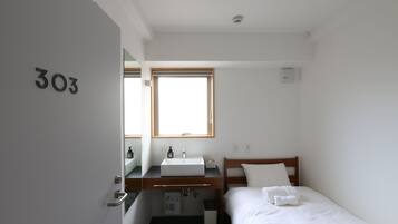 A small, clean room with a bed, a wooden desk with a sink, and a window.