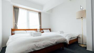 A hotel room with two single beds, a large window with curtains, a standing floor lamp, and a dark carpeted floor.
