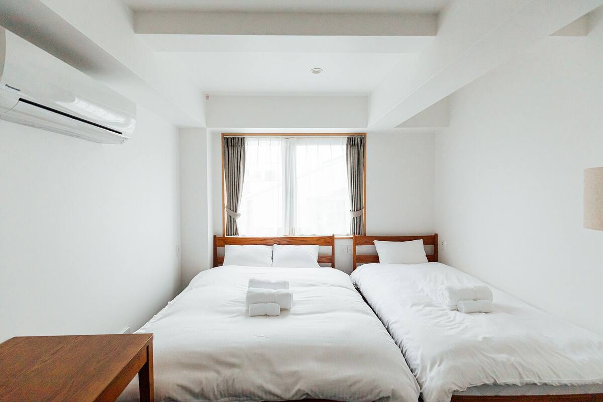 A hotel room with two beds, a wooden headboard, white bedding, and a window with curtains.