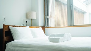 Una cama bien tendida con sábanas blancas, un cabecero de madera, una lámpara de noche y una ventana con cortinas.