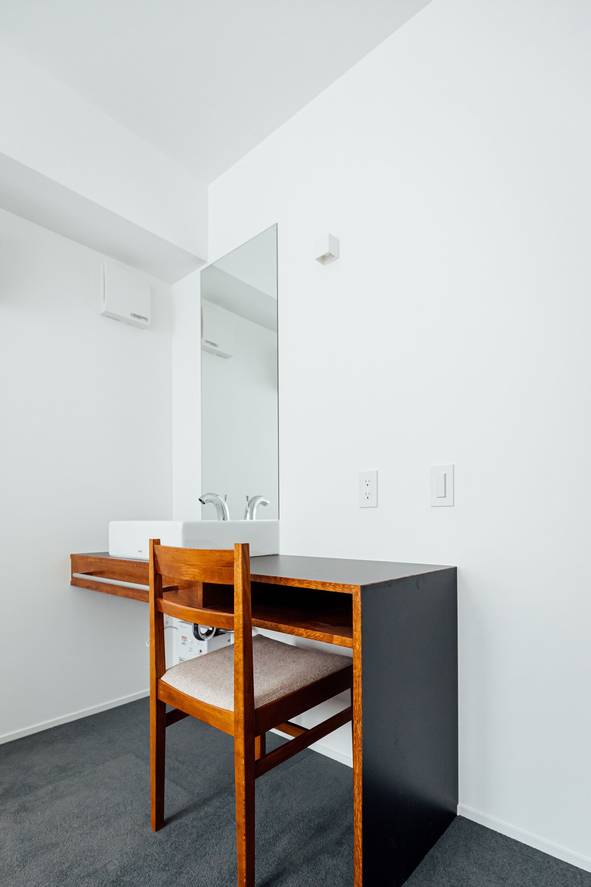 A modern bathroom with a wooden chair, a white sink, and a large mirror.