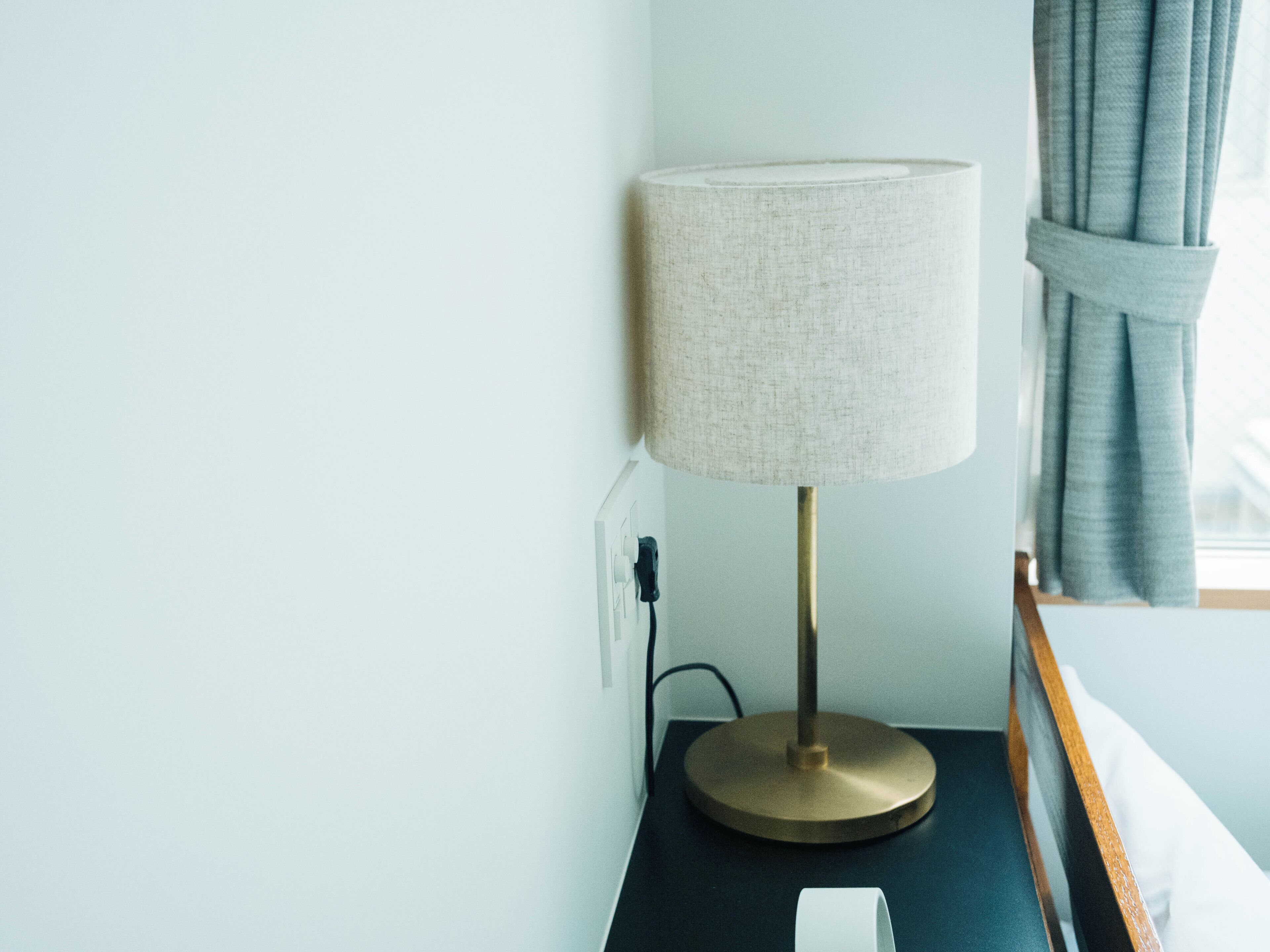 A bedside table with a lamp, a power outlet, and a window with curtains.
