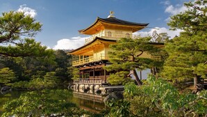 Un edificio tradicional japonés con un tejado escalonado, rodeado de exuberante vegetación y una masa de agua tranquila.