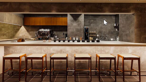 Un área de bar moderna con una barra alargada, varios taburetes y una máquina de café.
