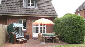 A patio with a table and chairs, a striped chair, and an umbrella. - Green area 33 flat 7 (Wyk auf Föhr)