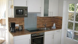 A compact kitchen with white cabinets, a microwave, a coffee maker, a kettle, and a sink. - Green area 33 flat 7 (Wyk auf Föhr)