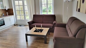 A modern living room with a brown sofa, a wooden coffee table, and a kitchen in the background. - Green area 33 flat 7 (Wyk auf Föhr)